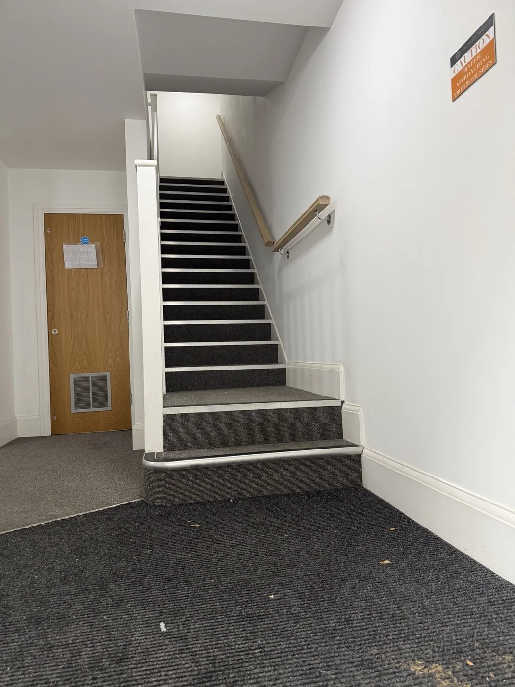 Timber handrails fitted along a communal stair flight and beside its lower landing and entrance steps.